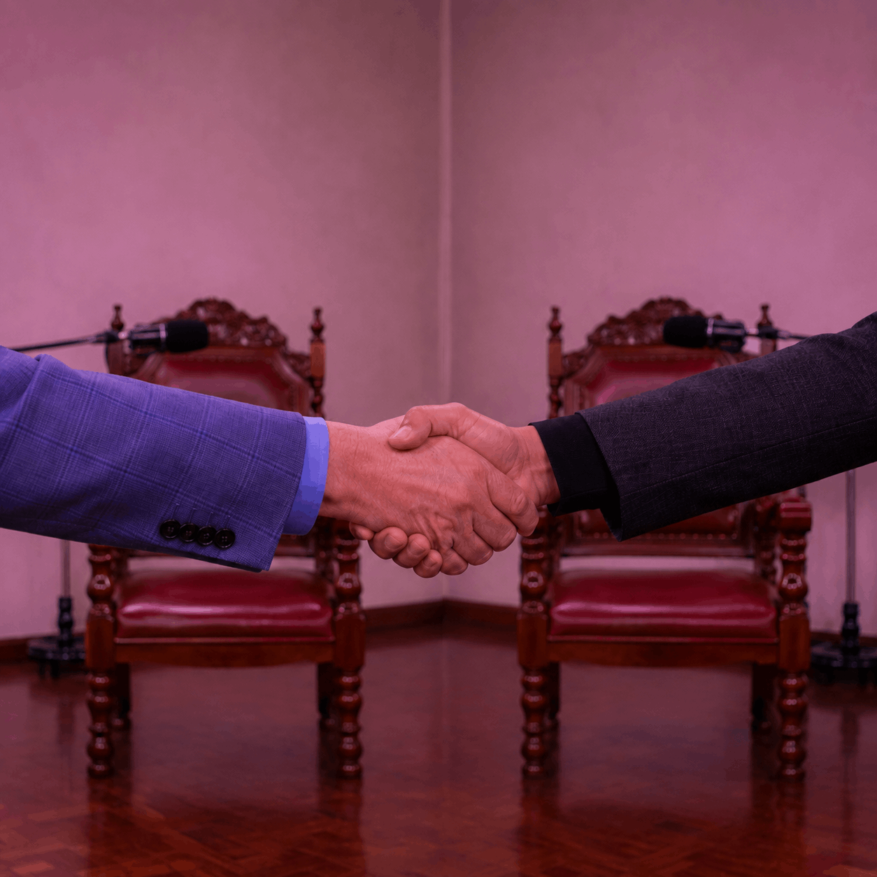 Saludo entre dos participantes frente a dos sillas y micrófonos de estudio